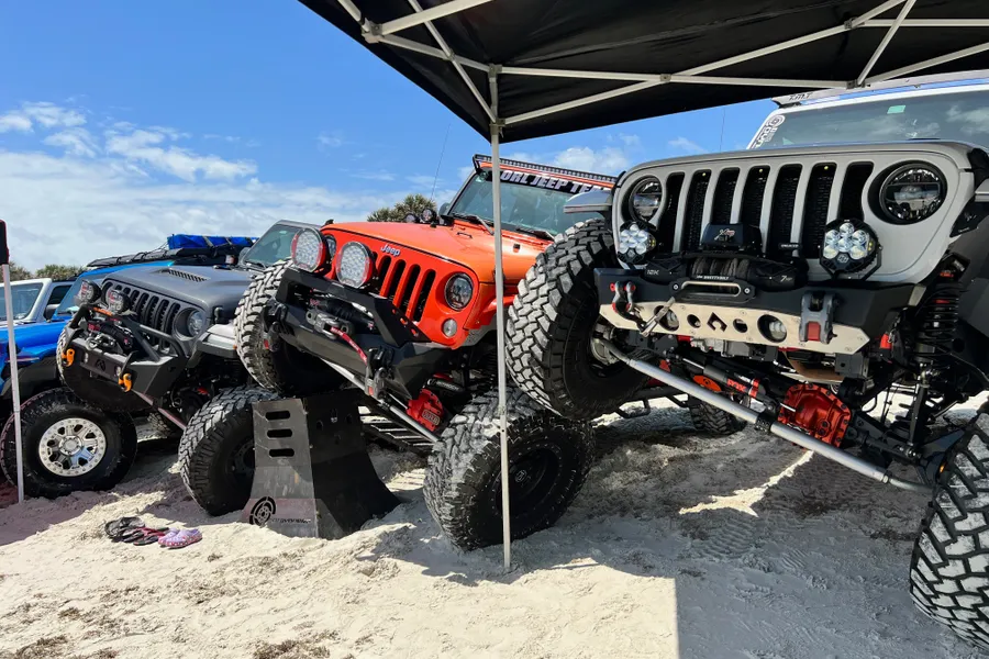 Lifted Jeeps showing off flex and suspension articulation on the sand under a canopy.