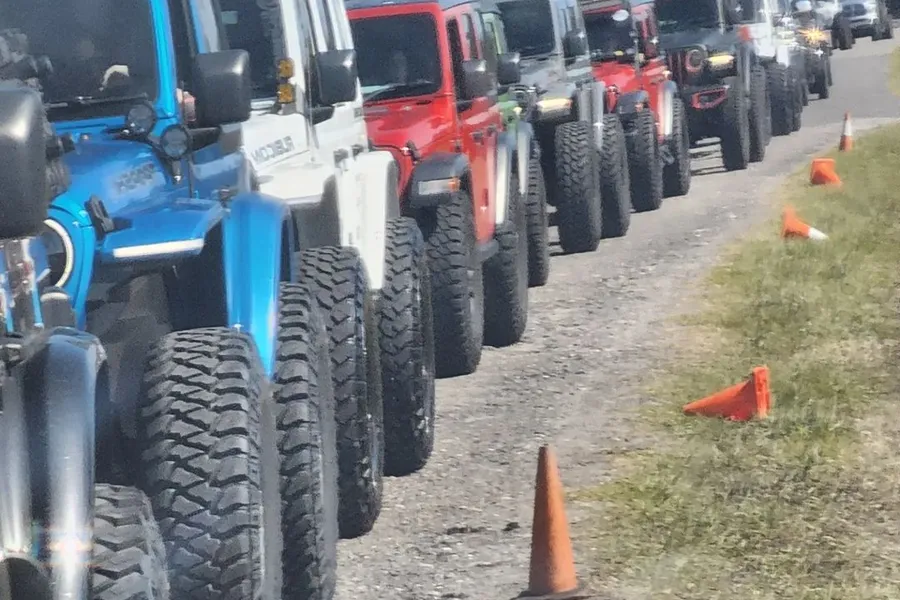 Row of Jeeps with large off-road tires lined up beside traffic cones on a dirt trail.