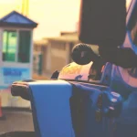 Close-up of a blue Jeep at sunset with blurred background showing a beach entrance booth and traffic cone.