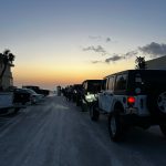 Line of Jeeps at sunset with a purple-orange sky and beach entrance in the distance.