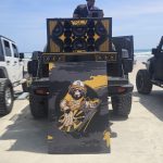 DJ Mr. Silent playing music from a Jeep outfitted with a custom sound system and a large illustrated poster on the beach.