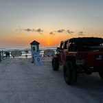 Red Jeep near a “Ramp Closed” sign at Volusia County beach ramp during sunset with ocean in the background.