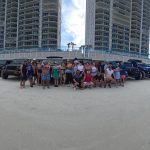 Panoramic photo of Orlando Jeep Team members in front of a row of Jeeps parked on Daytona Beach.